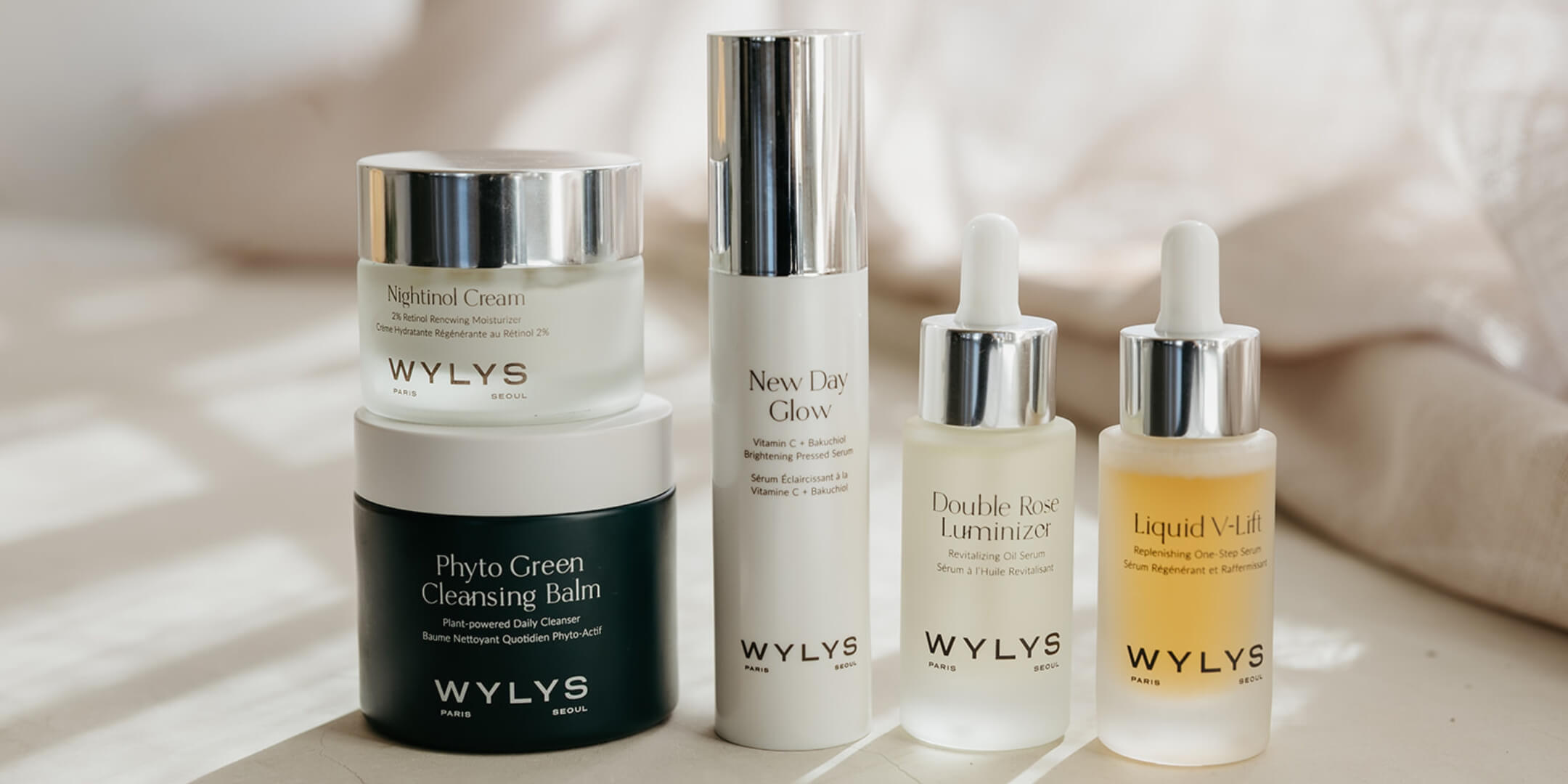 A horizontal lineup of WYLYS skincare featuring Phyto Cleanse Cleansing Balm, Nightfall Cream, New Day Glow, Double Rose Luminizer, and Liquid V-Lift.