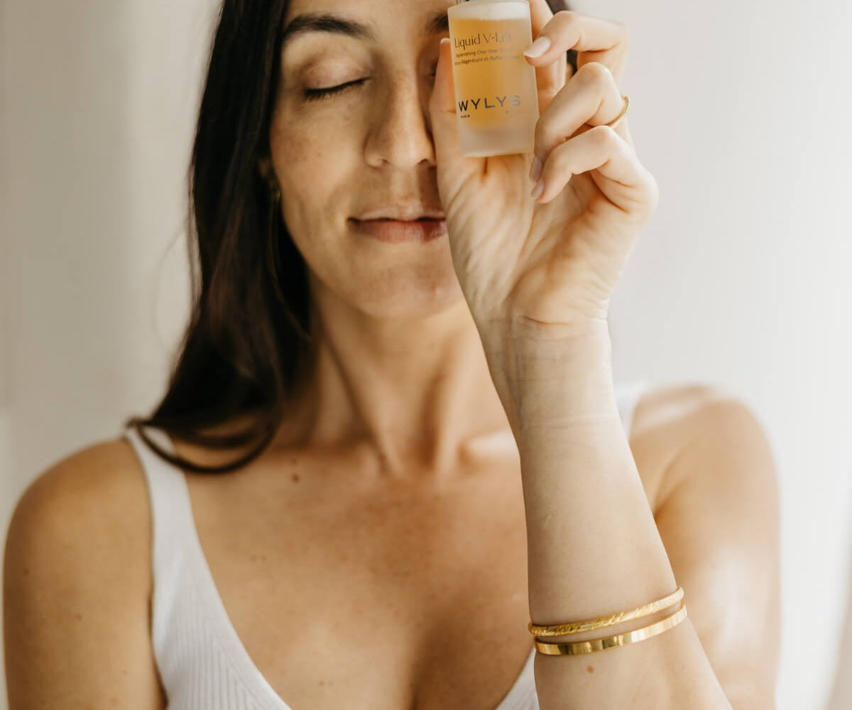 Woman holding a dropper with skincare product against a neutral background