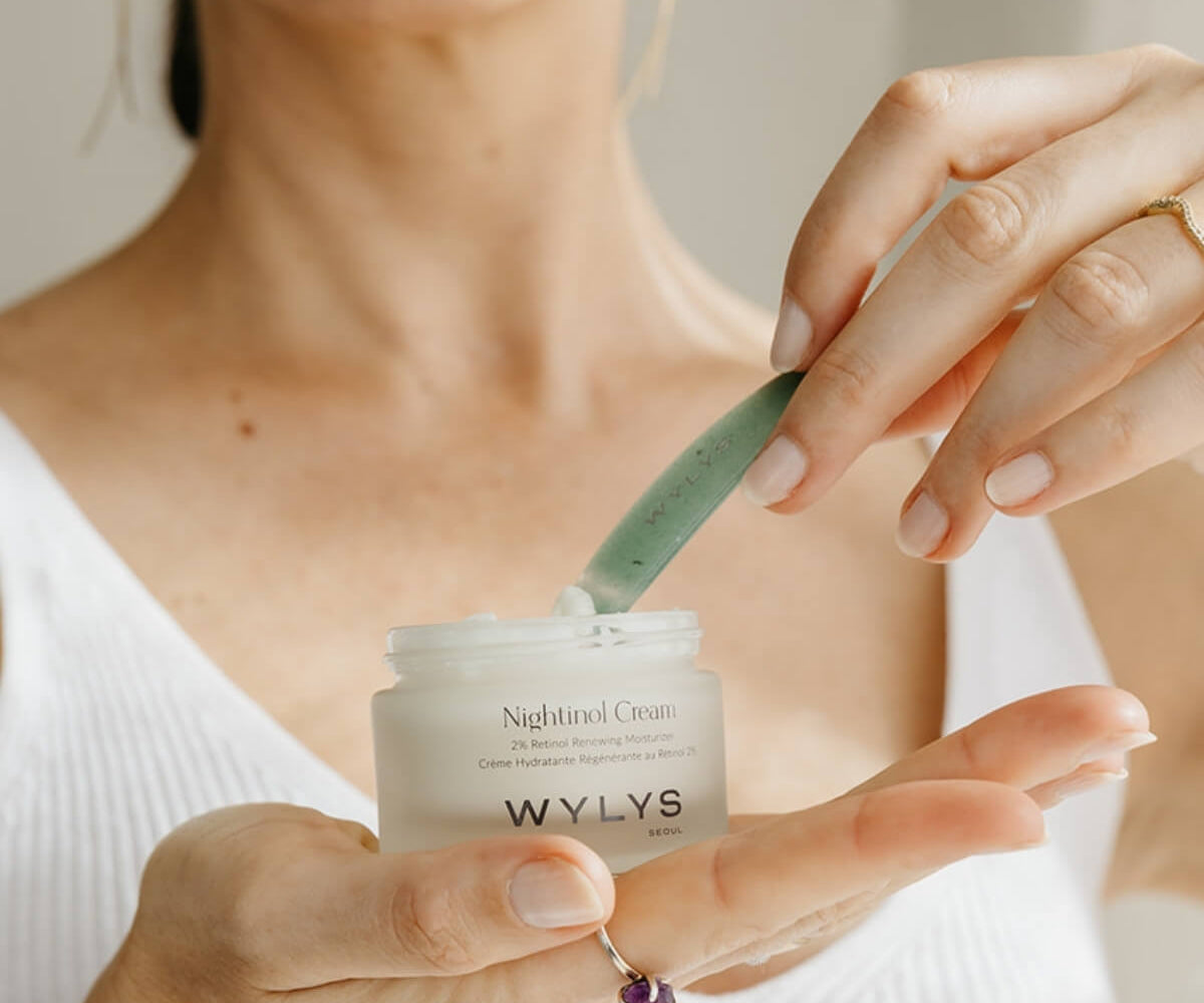 Person holding a jar of WYLYS night cream with a green applicator.