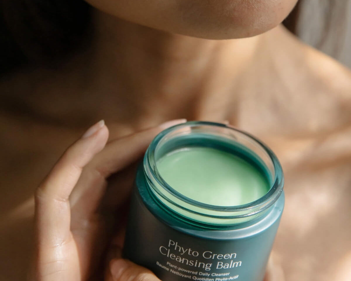 A person holding an open jar of WYLYS Phyto Green Cleansing Balm, highlighting the plant-powered green formula