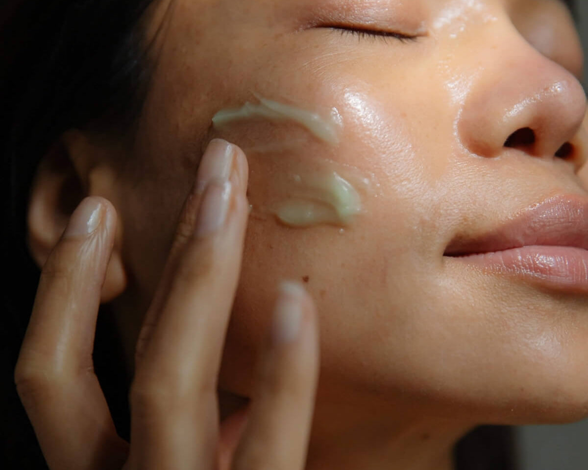 Close-up of a woman applying WYLYS Phyto Green Cleansing Balm to her cheek for a glowing complexion.