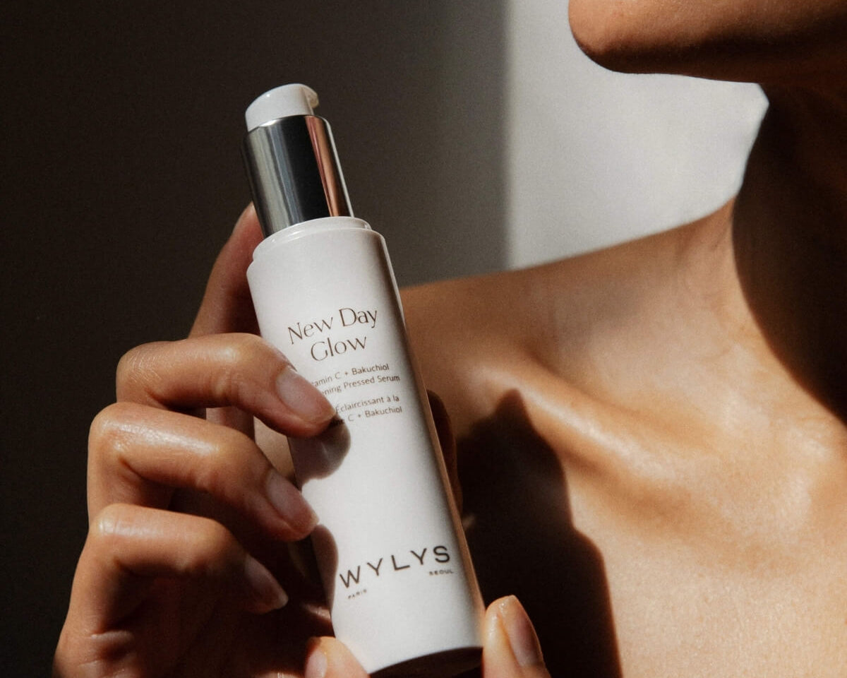 A woman holding the WYLYS New Day Glow Vitamin C + Bakuchiol Brightening Pressed Serum pump bottle.