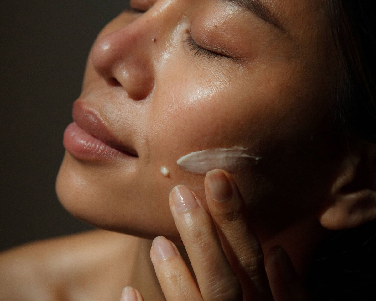 Close-up of a woman applying the creamy WYLYS New Day Glow serum to her face for skin brightening.