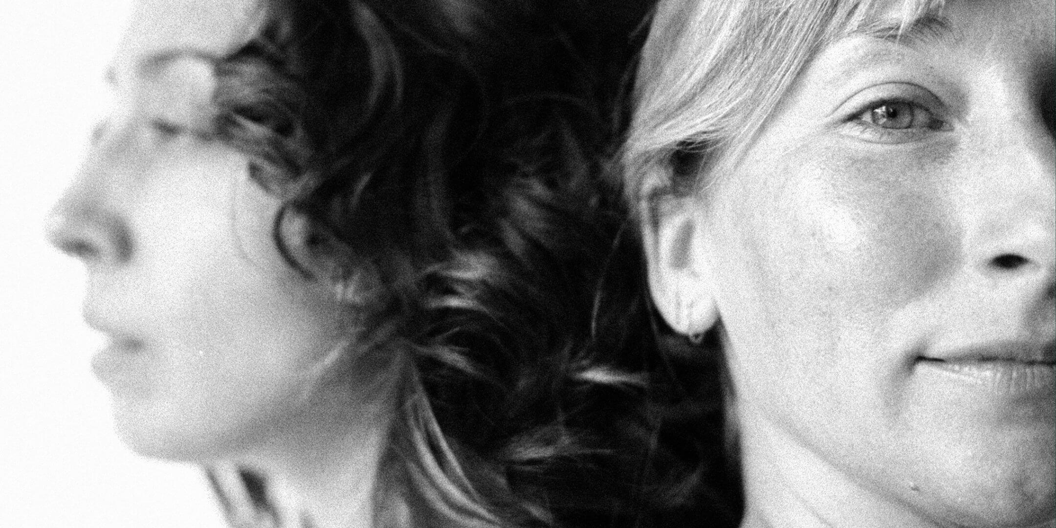 Black and white photo of two women, one with a blurred face and the other smiling.