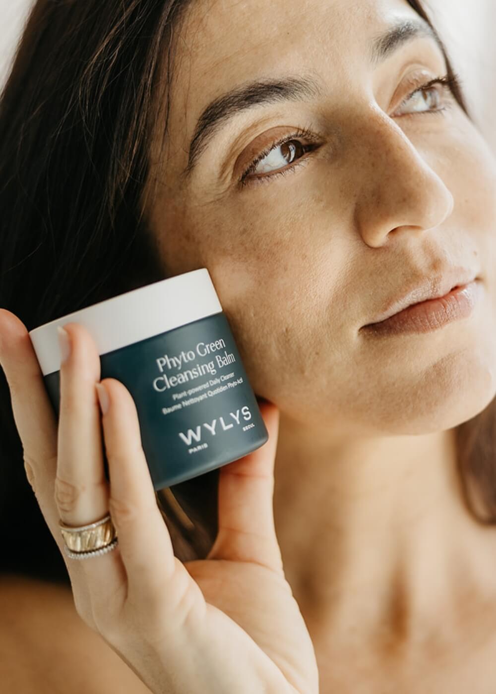 Woman holding a WYLYS Phyto Green Cleansing Balm jar close to her face.
