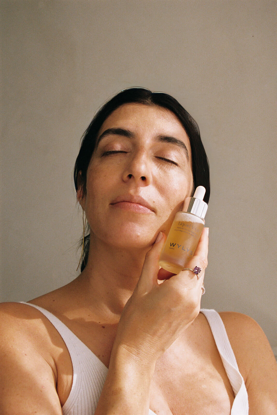 Woman applying skincare product to her face with a neutral background